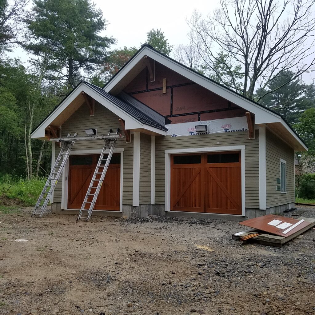 Two-bay garage with wood carriage doors and a standing-seam metal roof, ladders still up