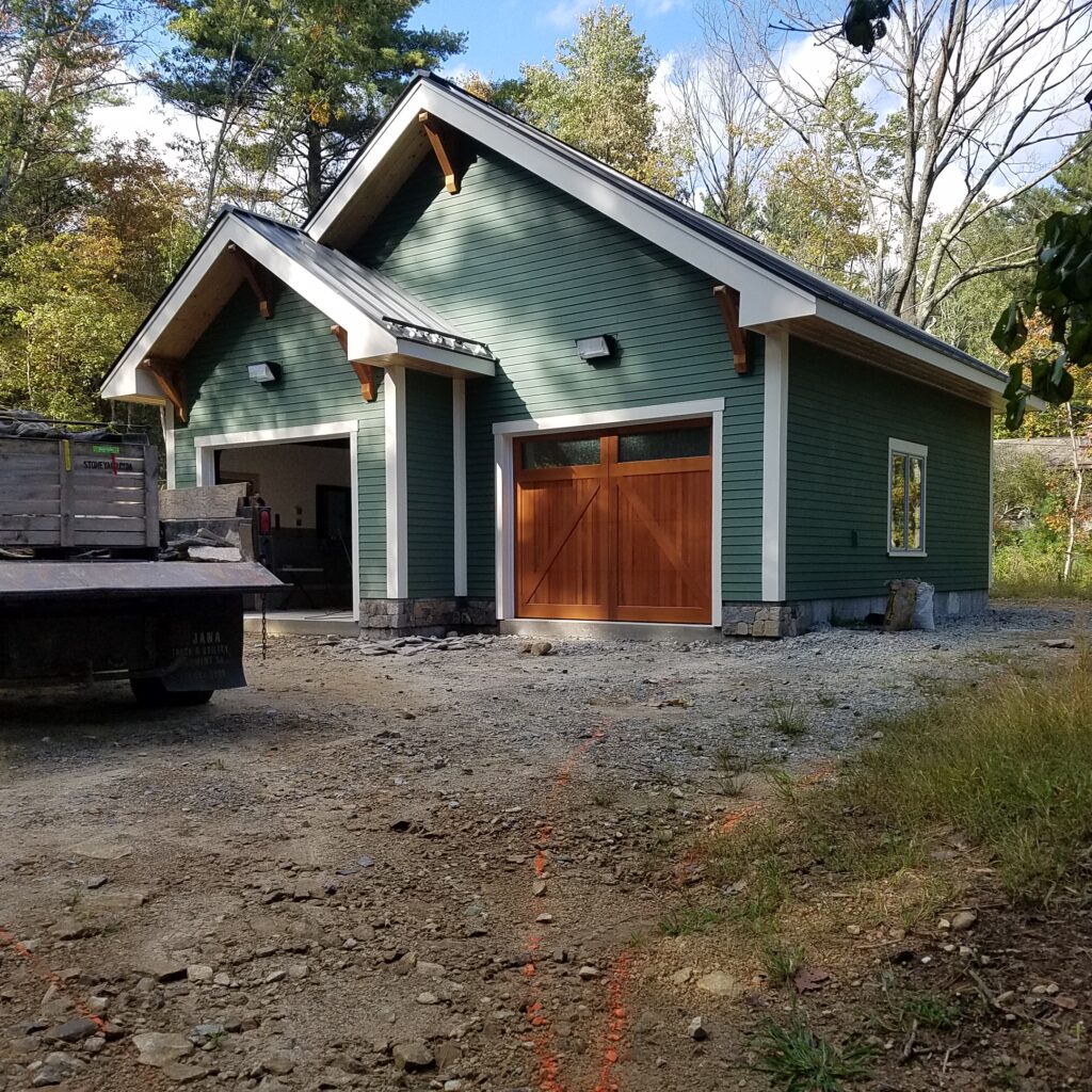 Green two-bay garage with a wood carriage door, nearly finished, with gravel in front