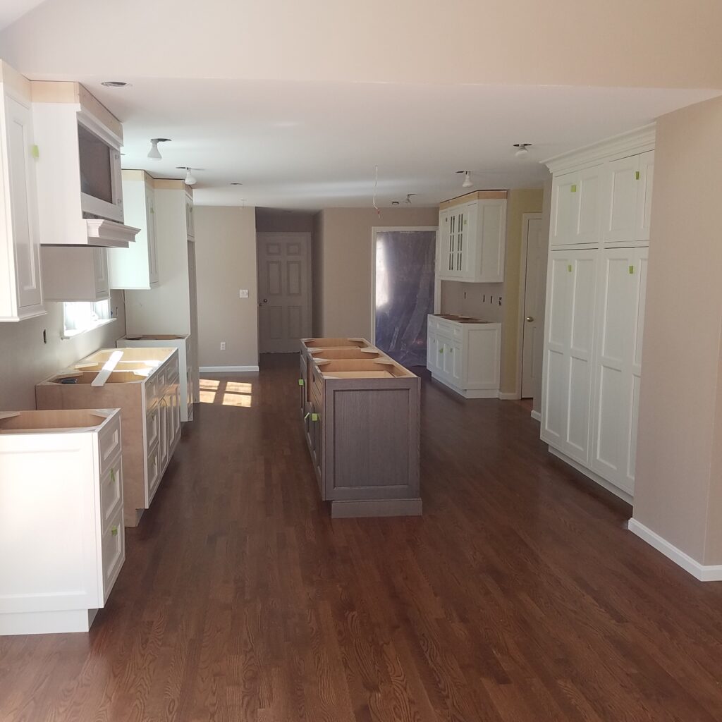 Kitchen nearing completion with white cabinets, a gray island and a new wood floor