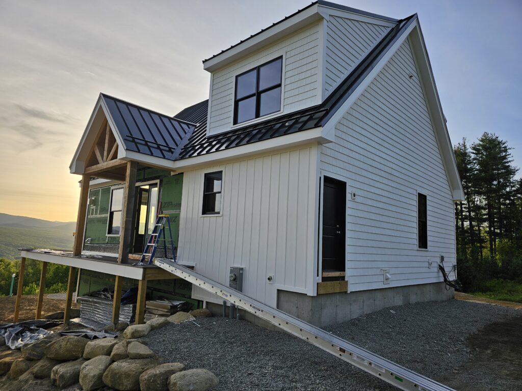 White board-and-batten addition with a black metal roof and a covered porch, photographed at dusk