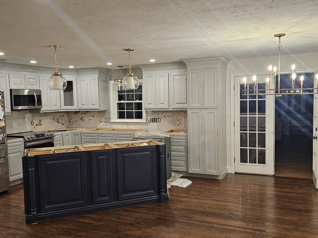 White cabinet kitchen with a navy island, pendant lights and a wood floor