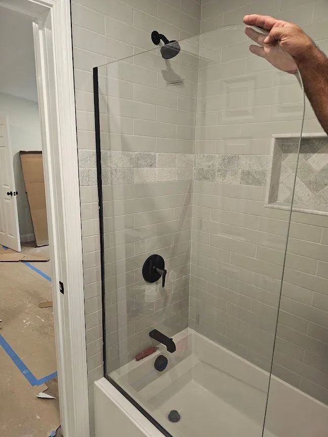 Tiled shower with black fixtures and a glass panel being installed