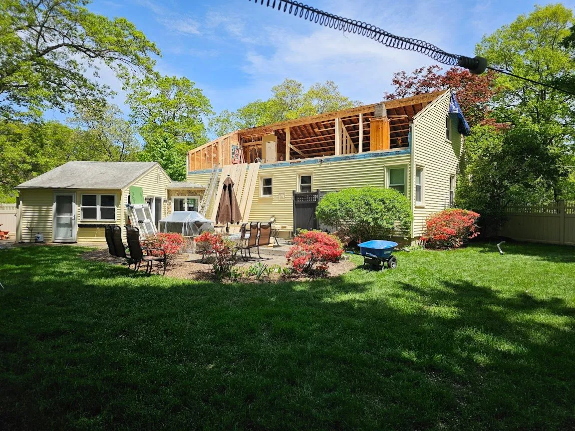 Second-story addition framed on top of a yellow-sided house, seen from the back yard