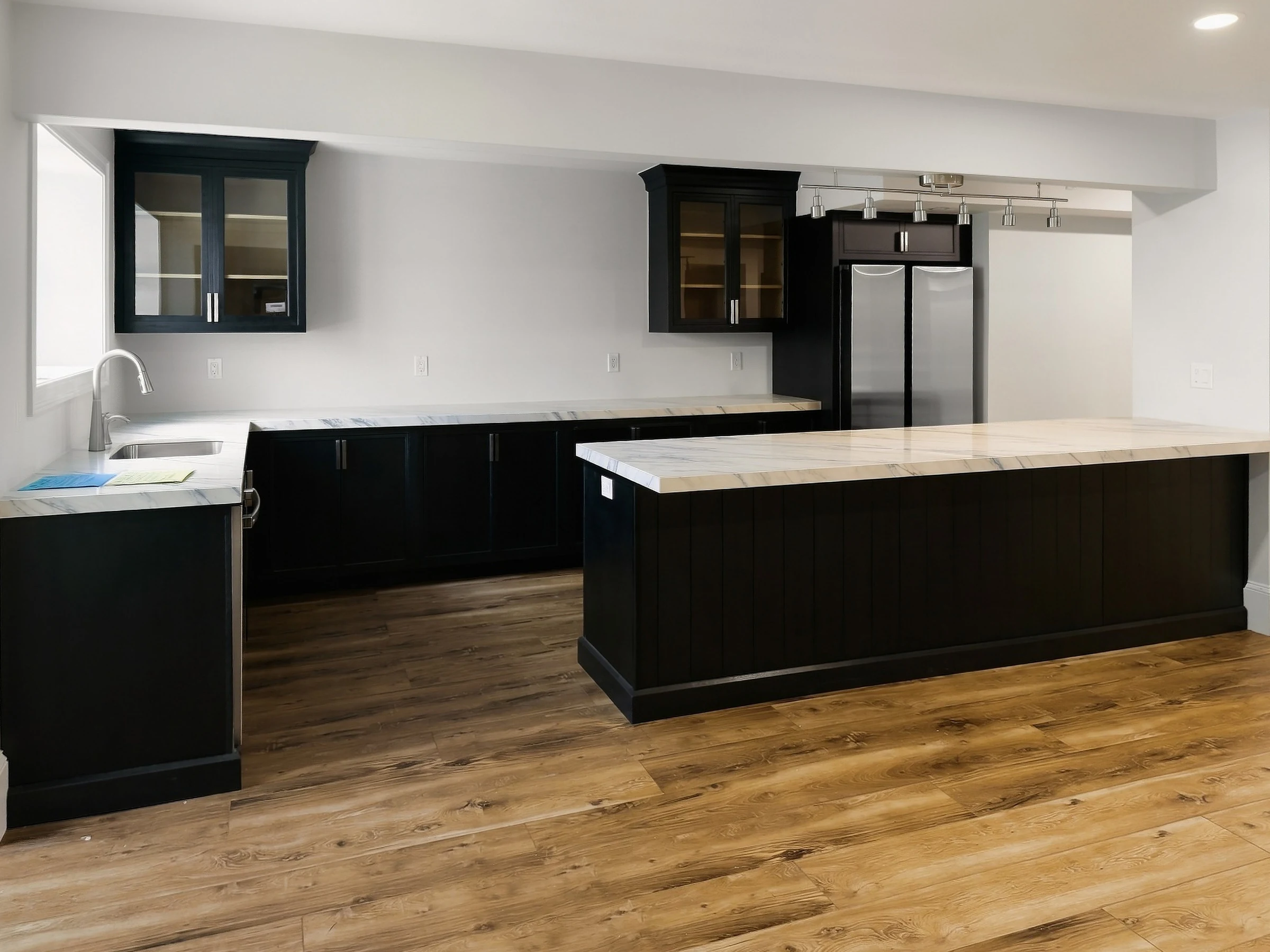 Lower-level kitchen with dark cabinetry, an island and wood-look flooring.