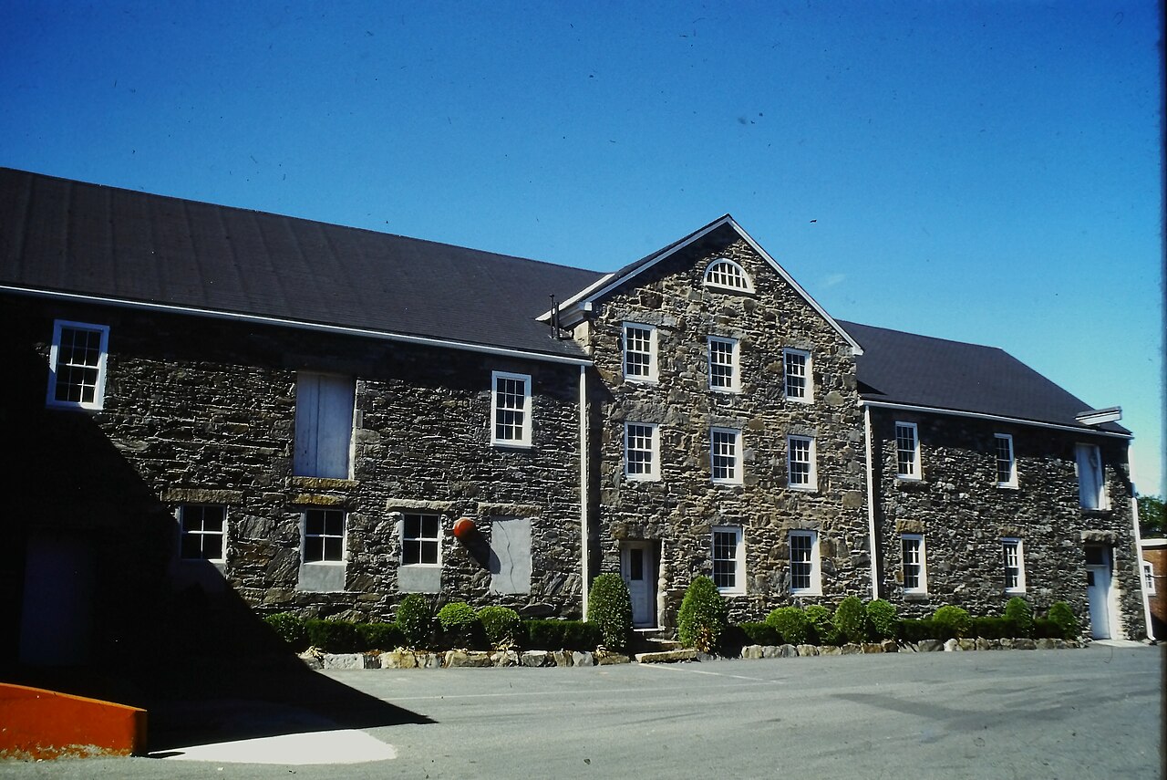 A long fieldstone mill building with a gable end, rows of white-trimmed windows and a dark roof