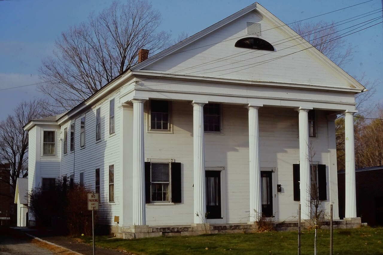 White Greek Revival house with a front portico of tall columns, black shutters and a side wing