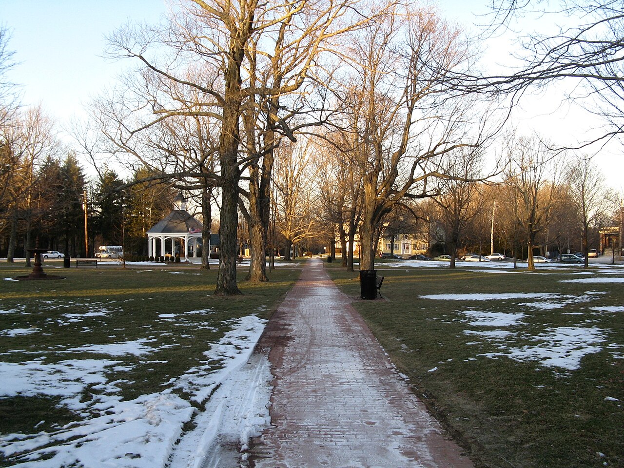 A paved path across the Hopkinton Town Common in winter, with bare trees, patches of snow and a gazebo in the distance