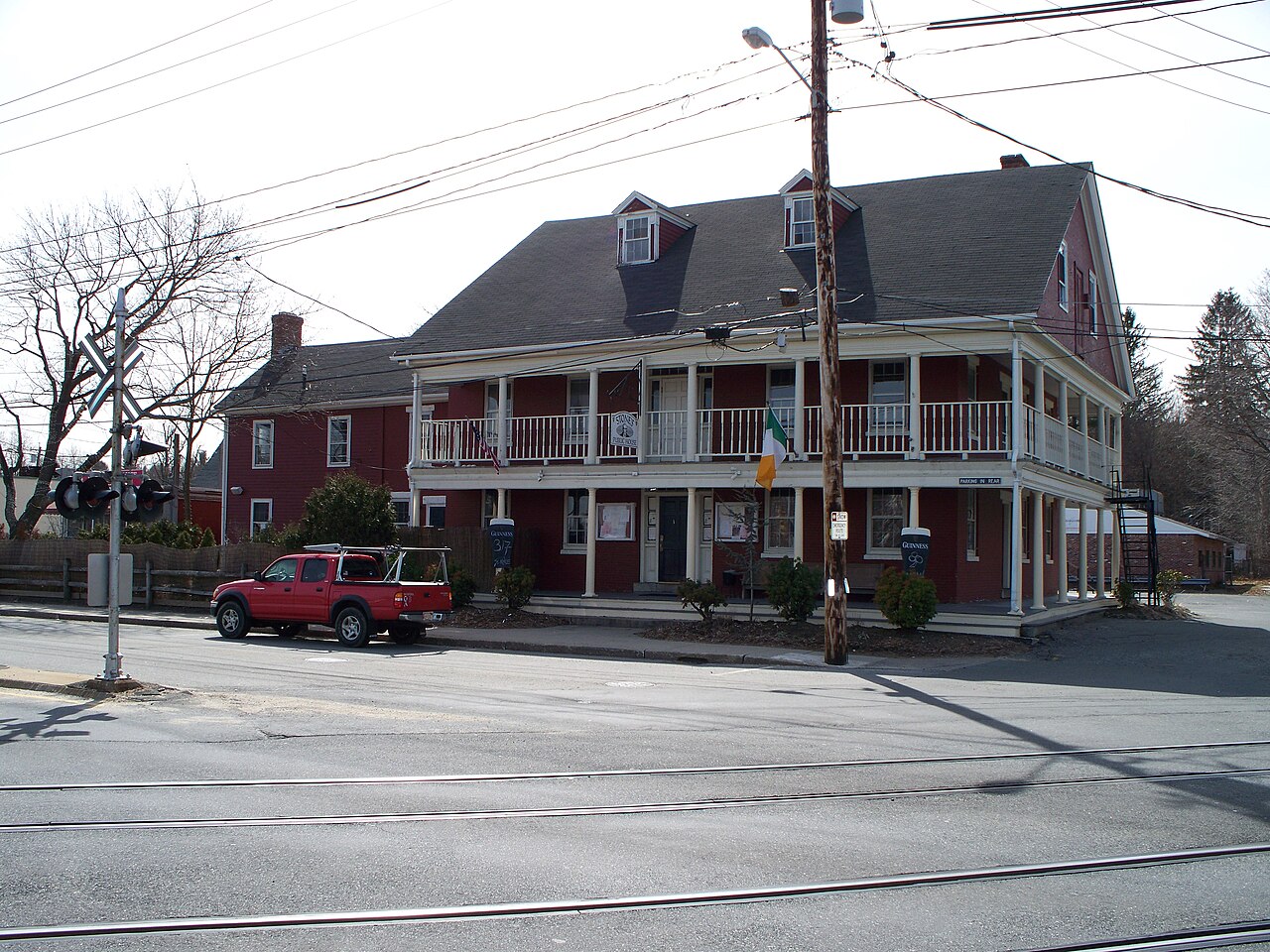A long red two-story inn with covered porches on both floors, beside railroad tracks