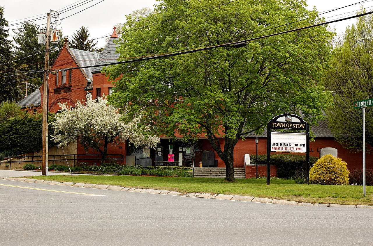 Brick library building behind a flowering tree and a Town of Stow sign on the green