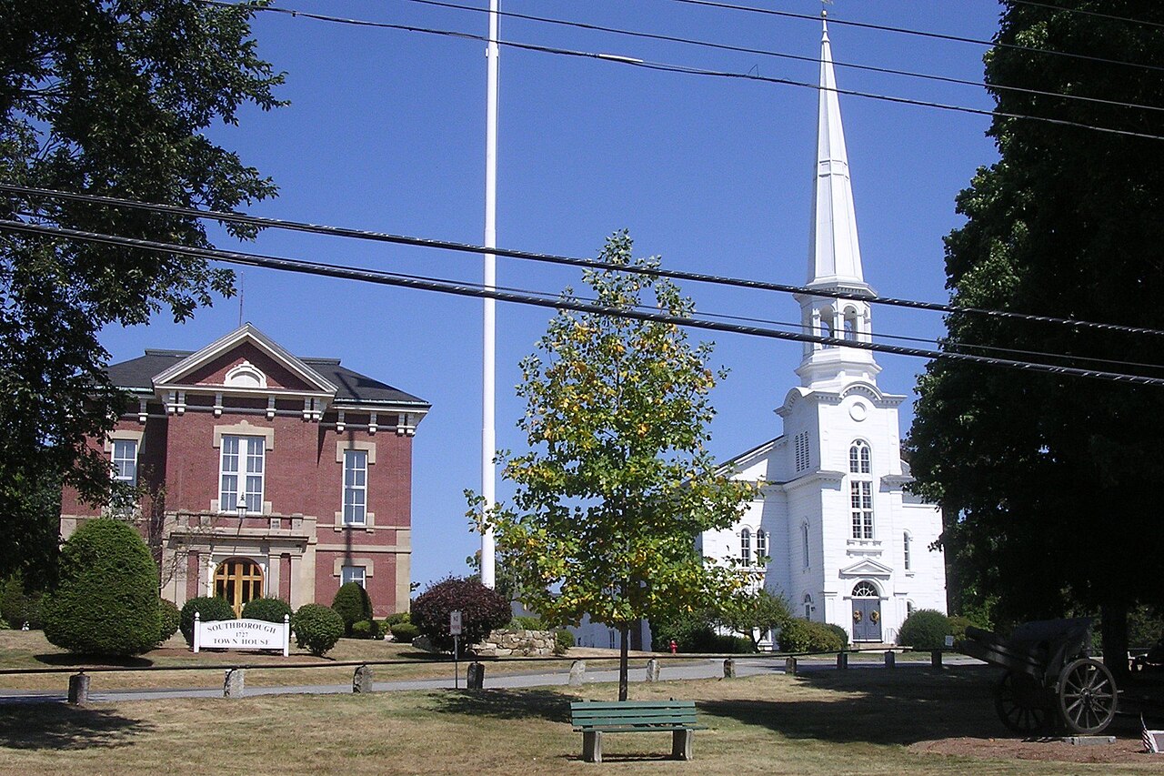 The brick Southborough Town House beside a white church with a tall steeple, seen across a lawn with a flagpole