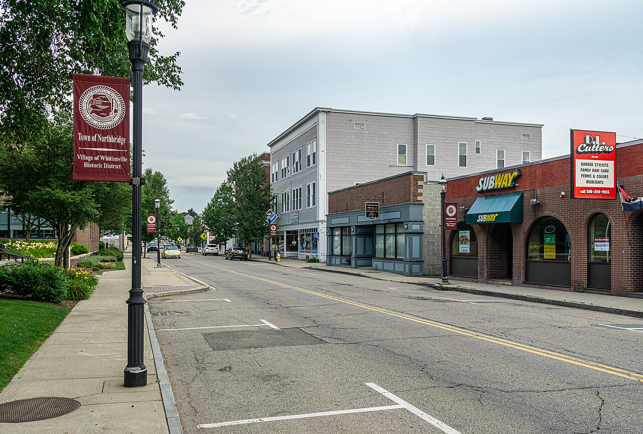 A street in Whitinsville with a Town of Northbridge historic district banner on a lamppost and storefronts along the road